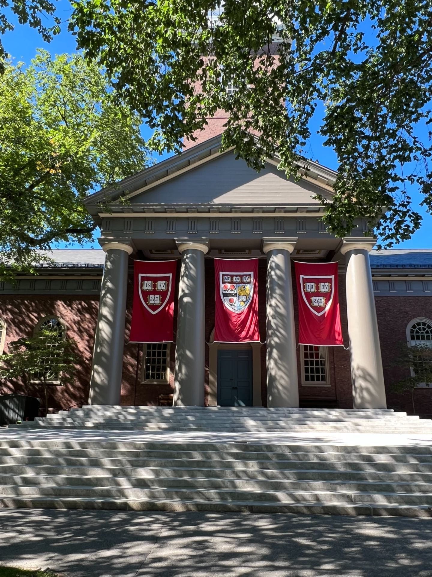 Front of a Harvard building with four columns and Harvard flags in between each column